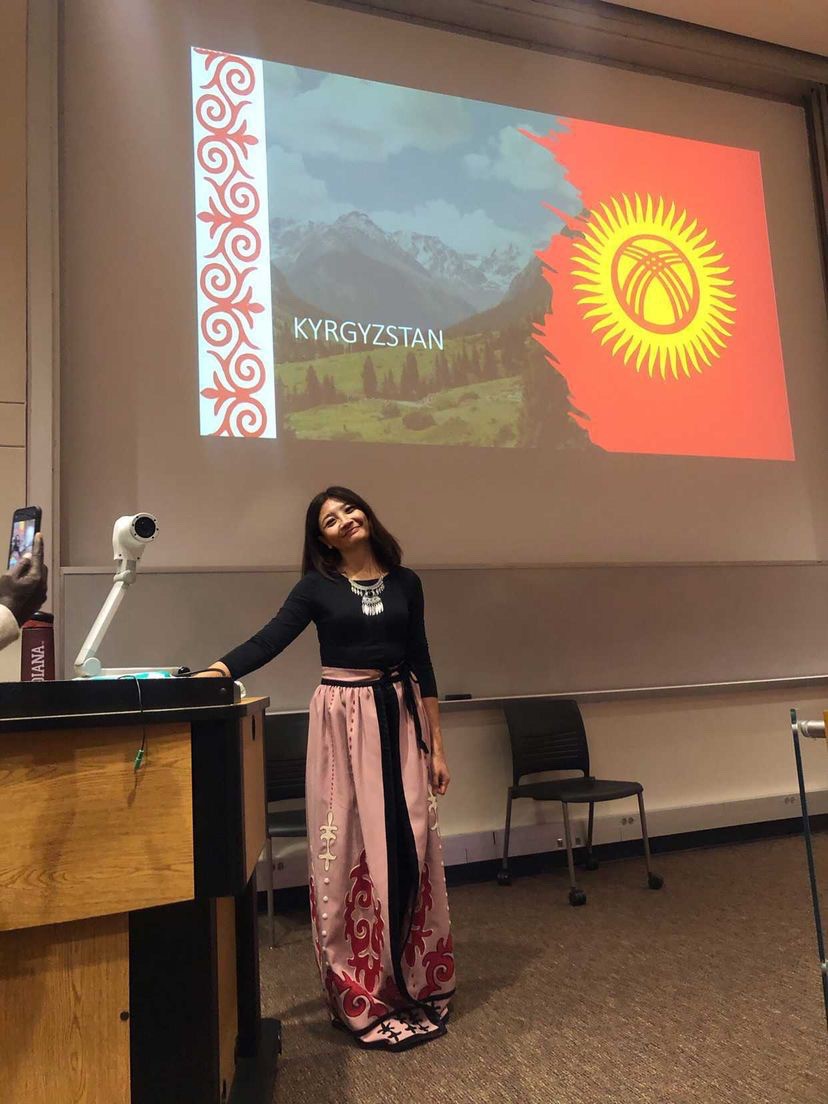 Woman doing speech in front of Kyrgyzstan powerpoint slideshow.